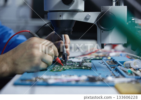 Electronics repair technician working under microscope 133606228