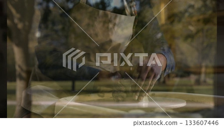 Female potter wearing apron shaping wet clay on pottery wheel at wooden table in park Female potter wearing apron shaping wet clay on pottery wheel at wooden table in park 133607446