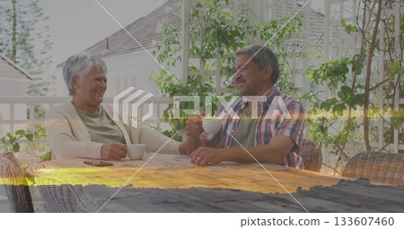 Sipping senior couple chatting on covered porch at table, with white ceramic mugs and smartphone Sipping senior couple chatting on covered porch at table, with white ceramic mugs and smartphone 133607460