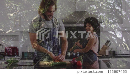 Man chopping vegetables and woman stirring pot wearing aprons in modern kitchen, with cutting board 133607463
