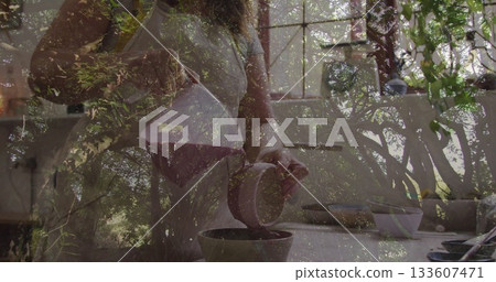 Woman wearing apron pouring coffee from ceramic carafe into mug at kitchen counter near window Woman wearing apron pouring coffee from ceramic carafe into mug at kitchen counter near window 133607471