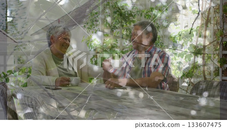 Sitting senior couple holding white coffee cups and checking phone on garden patio under pergola Sitting senior couple holding white coffee cups and checking phone on garden patio under pergola 133607475