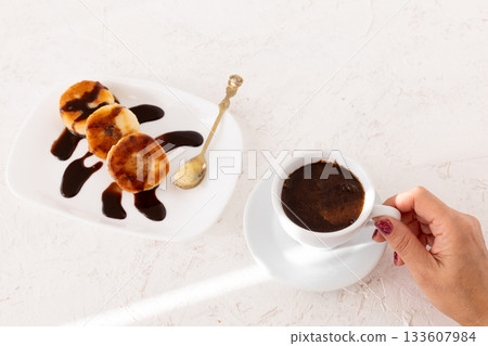Cup of coffee and curd fritters with chocolate on the porcelain plate. 133607984