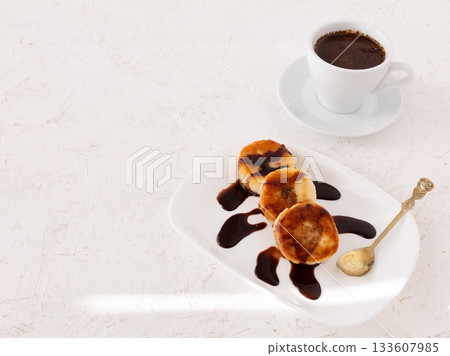 Curd fritters with chocolate on the porcelain plate and a cup of coffee. 133607985