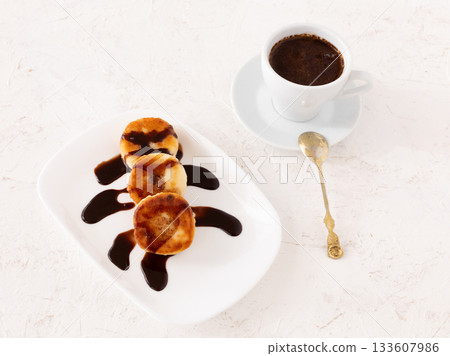 Curd fritters with chocolate on the porcelain plate and a cup of coffee. 133607986