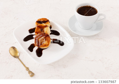 Curd fritters with chocolate on the porcelain plate and a cup of coffee. 133607987
