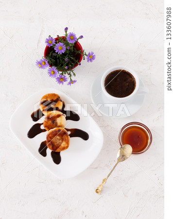 Curd fritters with chocolate on the porcelain plate and a cup of coffee. 133607988