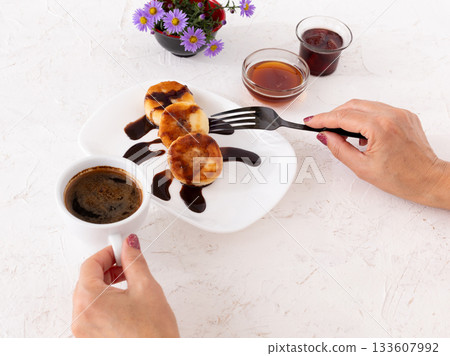 Woman with curd fritters on the porcelain plate and a cup of coffee. 133607992