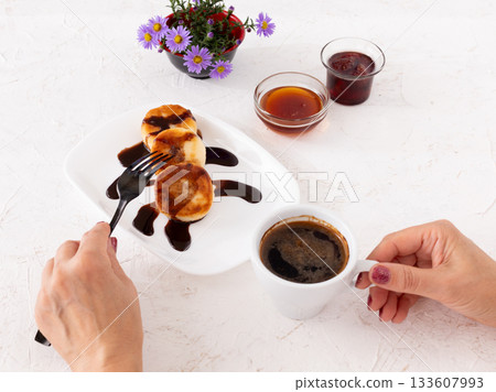 Woman with curd fritters on the porcelain plate and a cup of coffee. 133607993