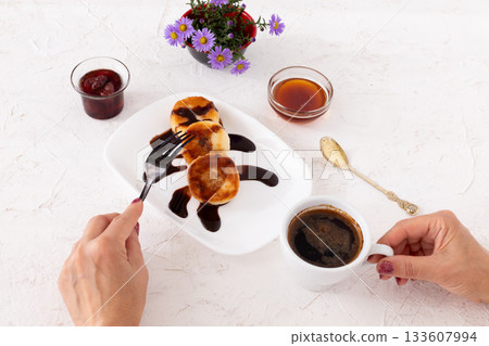 Woman with curd fritters on the porcelain plate and a cup of coffee. 133607994