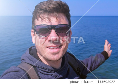 Man video chats selfie smartphone on sea beach waves hand greets and smiles. 133608022