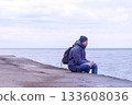 Man tourist sits on old sea waterfront and looks at sea in winter with phone. 133608036