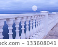 White balloon in the wind tied to the fence on sea waterfront in a cloudy day. 133608041