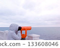 Woman in white jacket and hood looks in binoculars at sea waterfront with sea view. Side view. 133608046