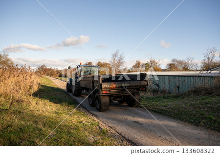 tractor with trailer driving on rural dirt road in autumn countryside tractor with trailer driving on rural dirt road in autumn countryside 133608322