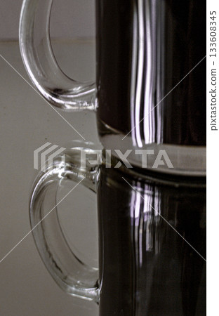 Thick glass mug with coffee and reflection in an old mirror Thick glass mug with coffee and reflection in an old mirror 133608345