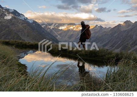 Hiker reflected in Sealy Tarns pool facing Mount Cook sunset, New Zealand Hiker reflected in Sealy Tarns pool facing Mount Cook sunset, New Zealand 133608625