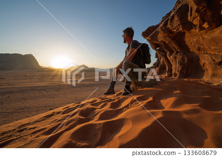 Male tourist sitting on rock ledge watching desert sunset, Wadi Rum, Jordan Male tourist sitting on rock ledge watching desert sunset, Wadi Rum, Jordan 133608679