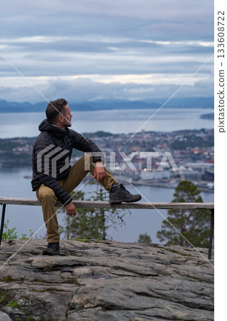Hiker sitting on bench overlooking Trondheim from Vattakammen, Norway Hiker sitting on bench overlooking Trondheim from Vattakammen, Norway 133608722