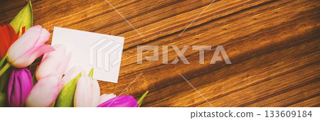 Colorful tulip bouquet and blank card are resting on flat design warm wooden tabletop, copy space 133609184