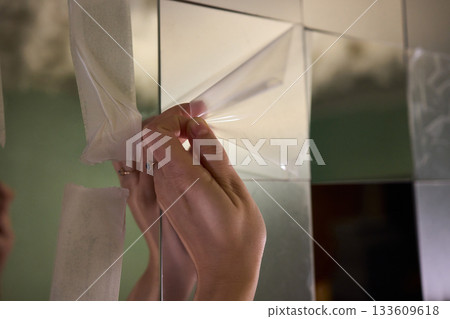 Removing protective layer to reveal clear glass, Carefully removing protective film from mirror to show pristine reflective surface in warm lit bathroom environment 133609618