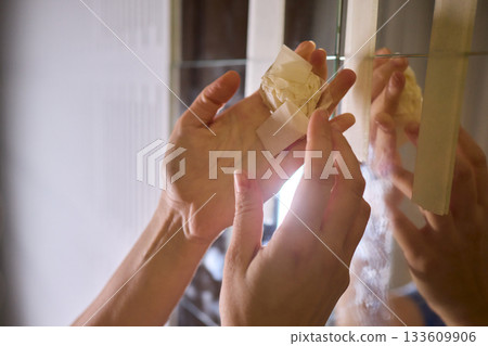Final touch on reflective surface, Applying sponge to seal mirror tape in home renovation, Using sponge to smooth and seal mirror edge during home makeover process 133609906