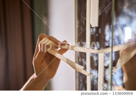 Mirror masking preparation, Detail oriented process of taping mirror for painting, Meticulous handwork involves aligning masking tape precisely on reflective glass surface 133609909