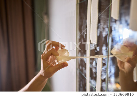 Mirror masking preparation, Detail oriented process of taping mirror for painting, Meticulous handwork involves aligning masking tape precisely on reflective glass surface Mirror masking preparation, Detail oriented process of taping mirror for painting, Meticulous handwork involves aligning masking tape precisely on reflective glass surface 133609910