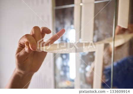 Mirror masking preparation, Detail oriented process of taping mirror for painting, Meticulous handwork involves aligning masking tape precisely on reflective glass surface 133609914