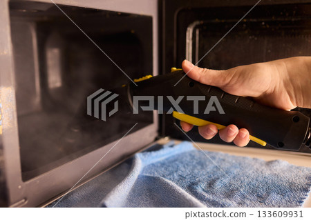 Cleaning microwave safely, Handheld steamer removes grime from microwave cavity efficiently, Ecofriendly steam cleaning method focuses on hygiene and appliance preservation 133609931