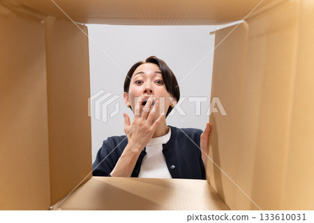 Woman looking into cardboard box, surprised Woman looking into cardboard box, surprised 133610031