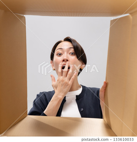 Woman looking into cardboard box, surprised Woman looking into cardboard box, surprised 133610033