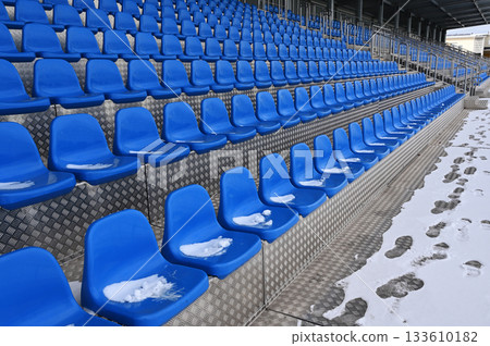 A row of blue plastic stadium seats, partially covered in snow 133610182