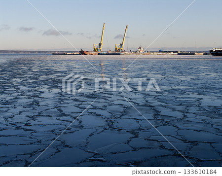 a frozen harbor with a vast cracked ice surface in the foreground 133610184