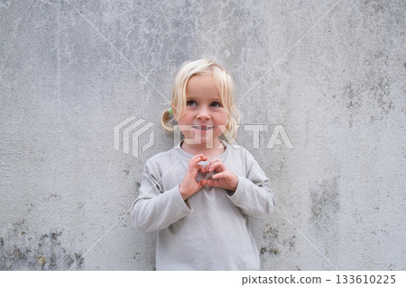 Little 4 Year Old Blonde Girl Standing by a Wall, Pretending to Be Angry and Showing Claws 133610225