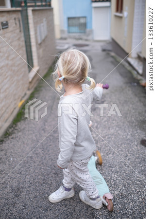 Little 4 Year Old Girl Walking Through Narrow Streets with a Scooter Without a Helmet Little 4 Year Old Girl Walking Through Narrow Streets with a Scooter Without a Helmet 133610227