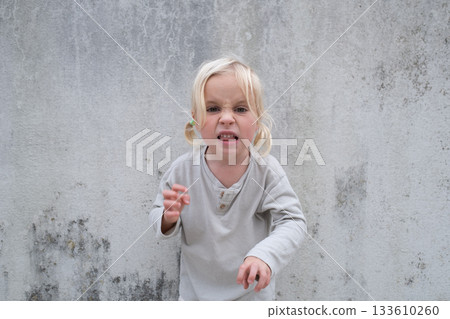 Little 4 Year Old Blonde Girl Standing by a Wall, Pretending to Be Angry and Showing Claws Little 4 Year Old Blonde Girl Standing by a Wall, Pretending to Be Angry and Showing Claws 133610260
