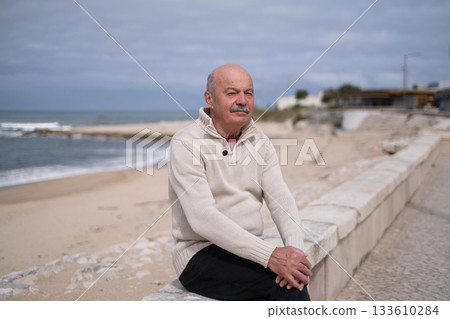 Elderly man with a mustache sitting on a seawall by the ocean Elderly man with a mustache sitting on a seawall by the ocean 133610284