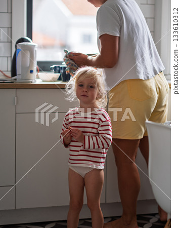 Little girl standing in the kitchen trying to get her mother attention 133610312