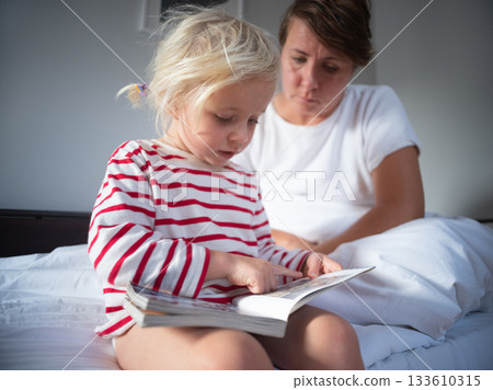 4 year old girl reading a book to her tired mother who is listening 133610315