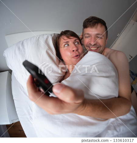 Married couple lying in bed looking at the phone with excitement. Married couple lying in bed looking at the phone with excitement. 133610317