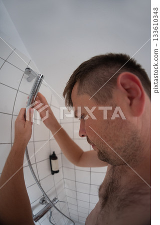 Man standing under a shower with no water, affected by water outage at home 133610348
