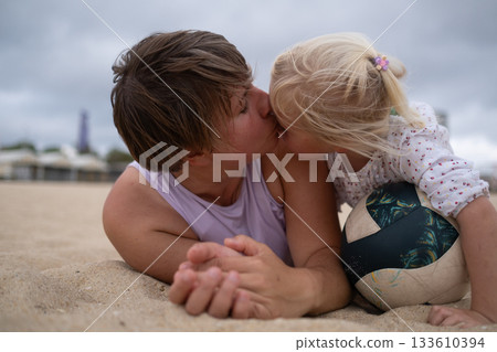Woman in sportswear relaxing on the beach with her daughter on the sand.  133610394