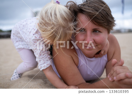 Woman in sportswear relaxing on the beach with her daughter on the sand.  133610395