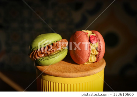 Two gourmet macarons with creative fillings, green with caramelized nuts and red with raspberry pieces and cream Two gourmet macarons with creative fillings, green with caramelized nuts and red with raspberry pieces and cream 133610600