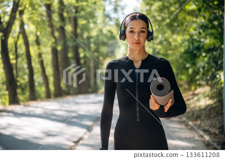 Model is with yoga mat. Young sportive skinny woman is in black fitness clothes outdoors 133611208