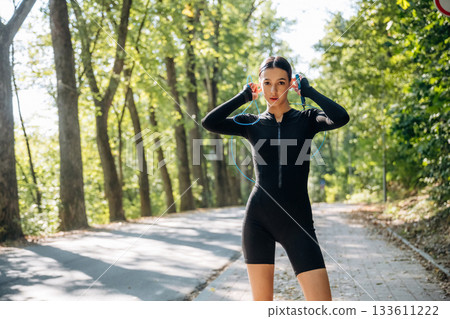 Blue jumping rope, standing with it. Young sportive skinny woman is in black fitness clothes outdoors Blue jumping rope, standing with it. Young sportive skinny woman is in black fitness clothes outdoors 133611222