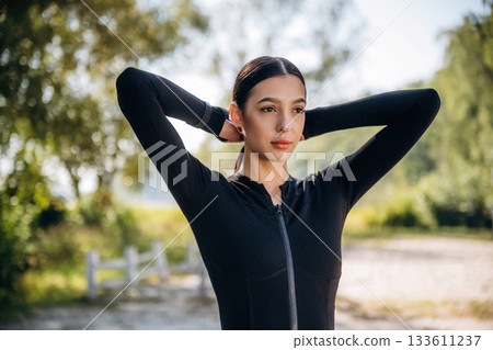 Making the ponytail, preparing for exercises. Young sportive skinny woman is in black fitness clothes outdoors 133611237