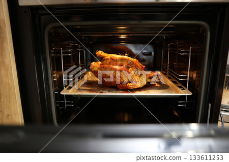 Festive christmas roast whole duck on aluminized steel baking sheet inside open oven at home kitchen. Ready golden turkey or goose on tray. Classic American Thanksgiving food preparation. 133611253