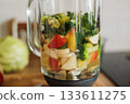 Glass blender bowl with apple, banana and broccoli slices, parsley and water inside on a wooden table on home kitchen. Healthy detox smoothie drink and lifestyle diet. Pieces of fruit ingredients. 133611275